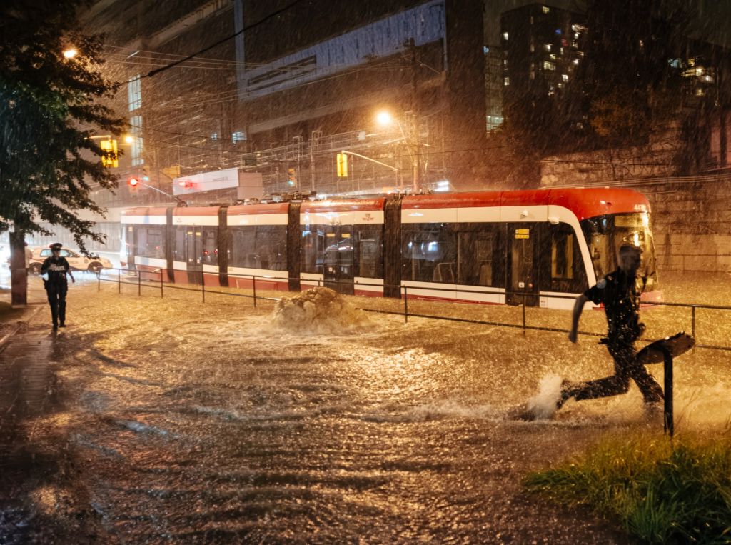 Flooded city street with a streetcar stuck in the water while two police officers run nearby.